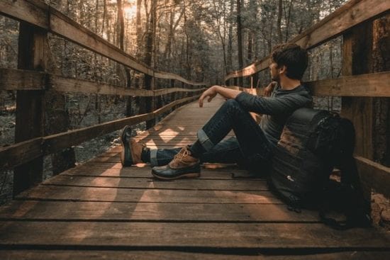 a man is sitting on a wooden bridge in the woods .