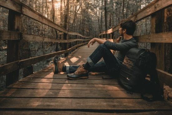 a man is sitting on a wooden bridge in the woods .