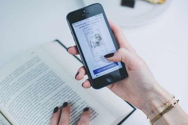 a woman is holding a cell phone in her hand while reading a book .