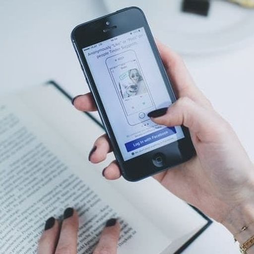 a woman is holding a cell phone in her hand while reading a book .