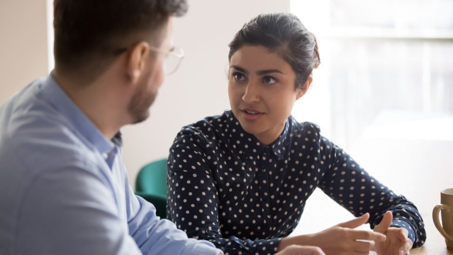a man and a woman are sitting at a table having a conversation .