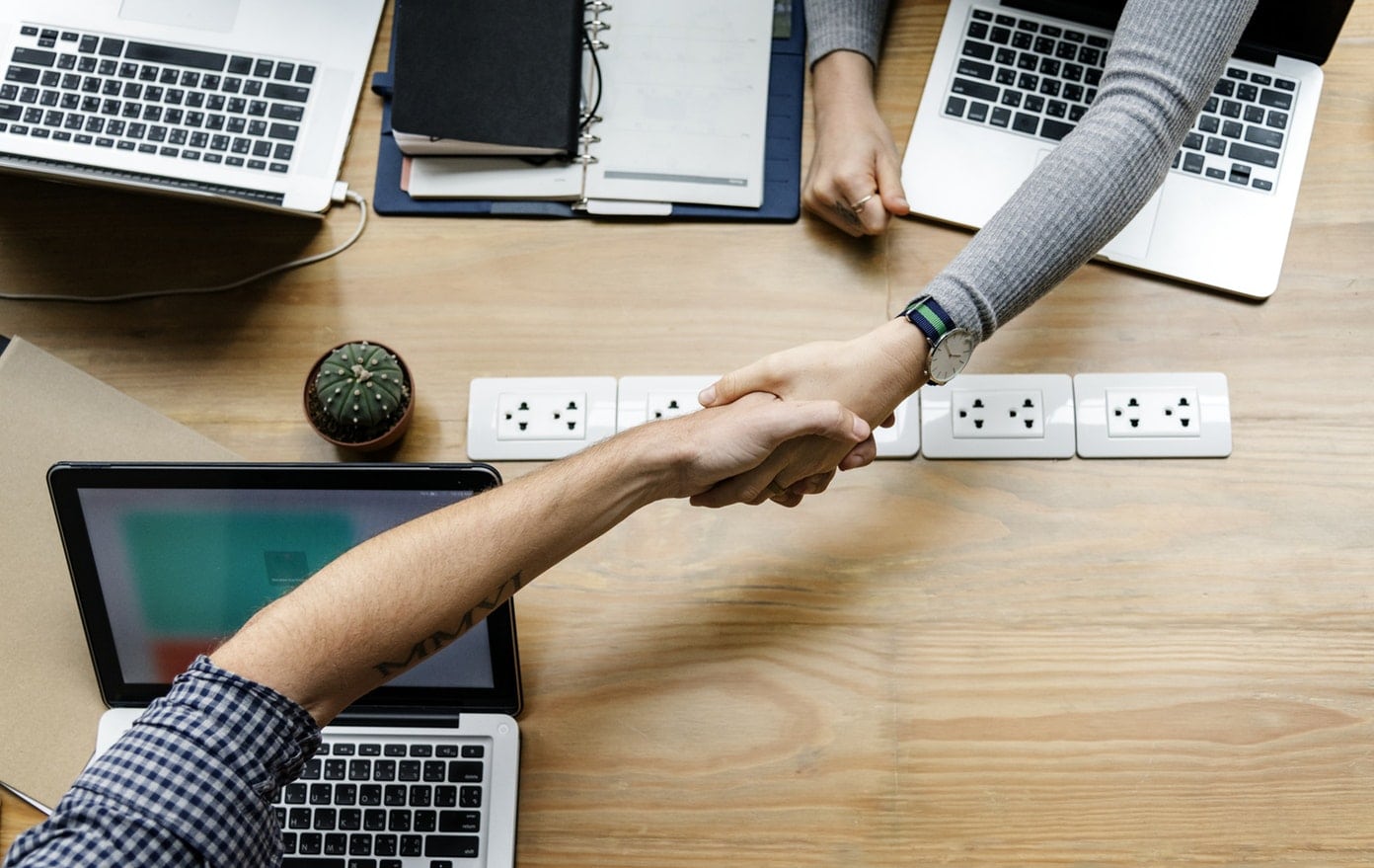 a man and a woman are shaking hands over a table with laptops .