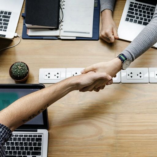 a man and a woman are shaking hands over a table with laptops .