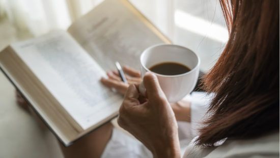 a woman is holding a cup of coffee while reading a book .