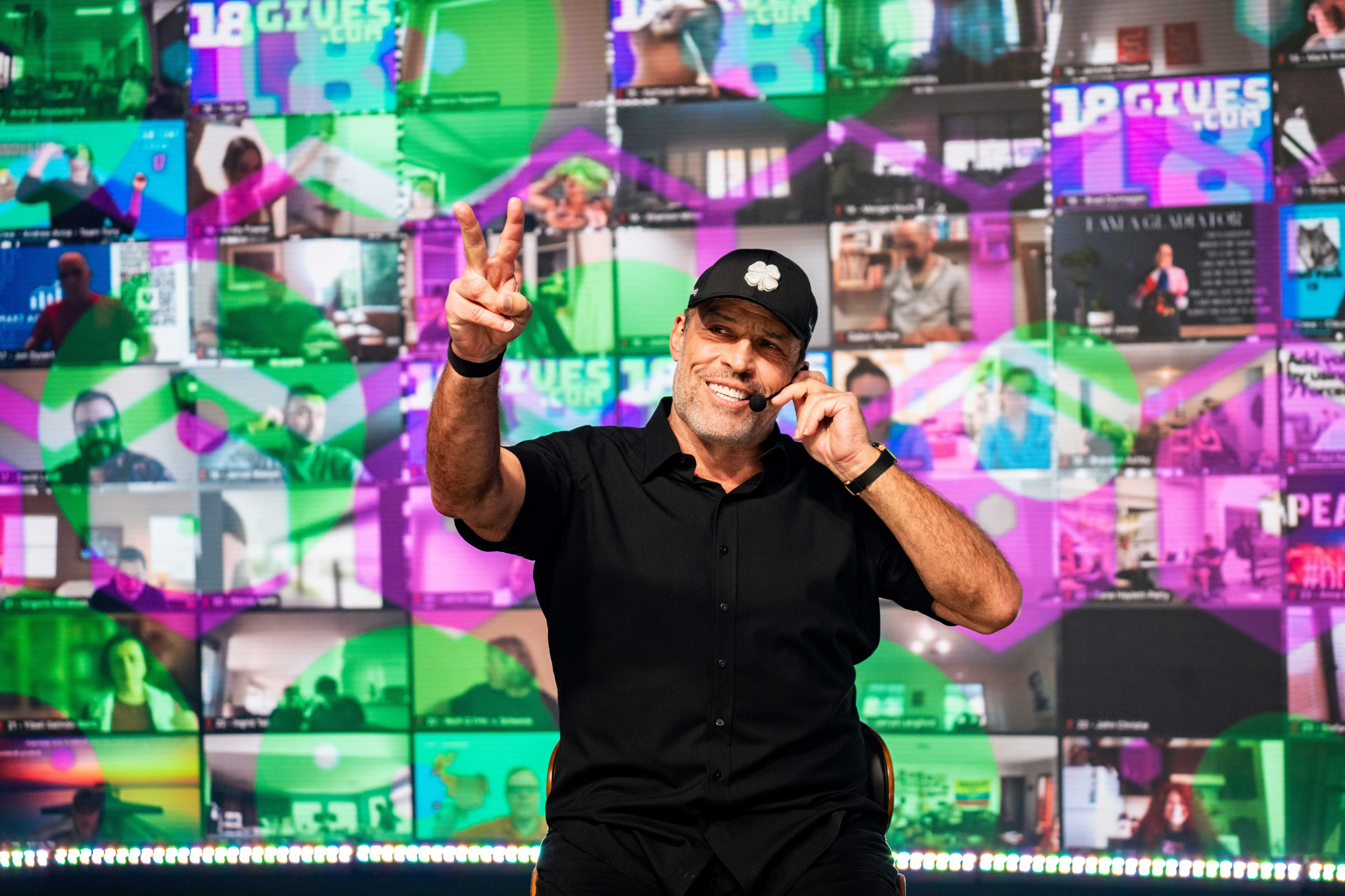 a man is giving a peace sign in front of a wall of television screens .