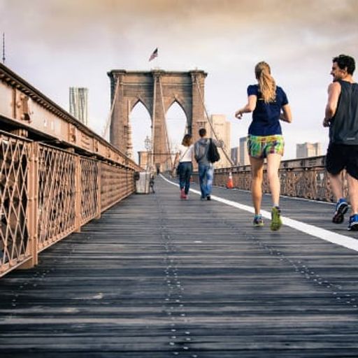 a group of people are running on a bridge in new york city .