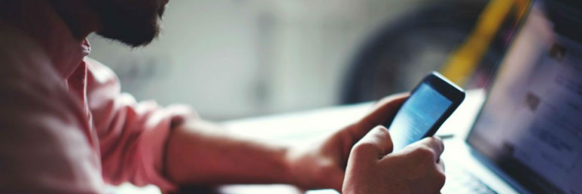 a man is sitting at a table using a cell phone .