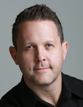 a man is standing in front of a brick wall with his hands in his pockets .