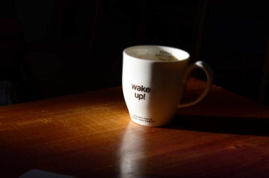 a white coffee mug with the words `` wake up '' written on it is sitting on a wooden table .