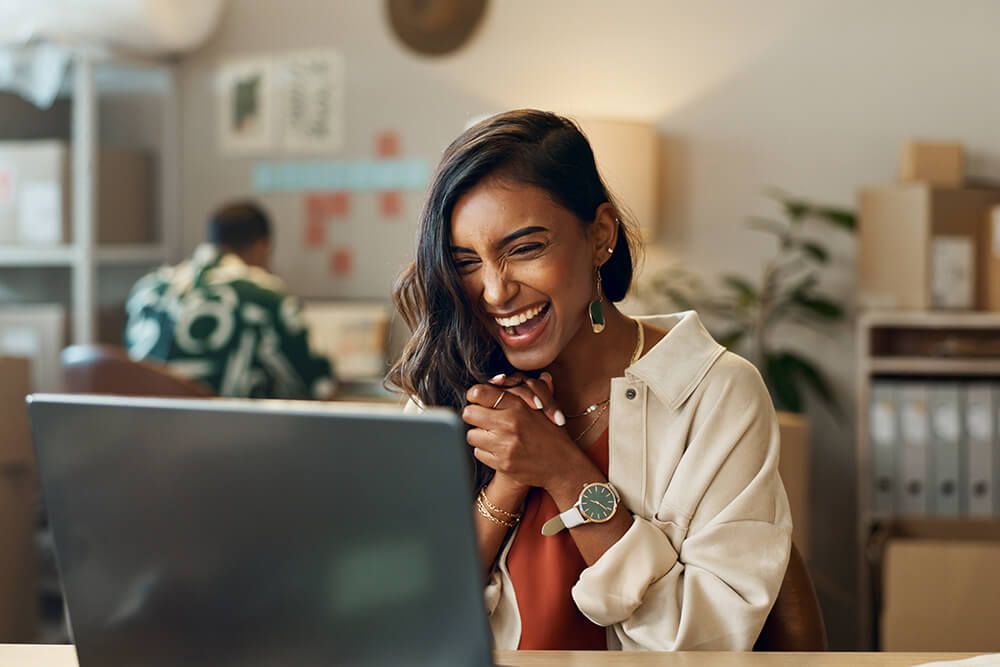a woman is laughing while looking at a laptop computer .