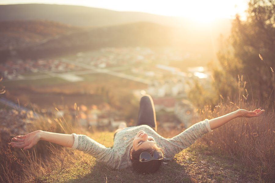 a woman is laying on a hill with her arms outstretched .