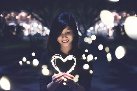 a woman is holding a heart made of lights in her hands .