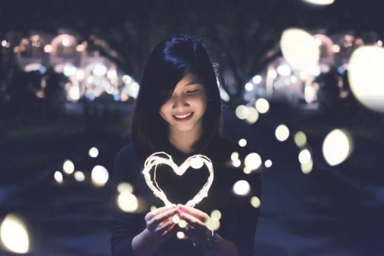a woman is holding a heart made of lights in her hands .