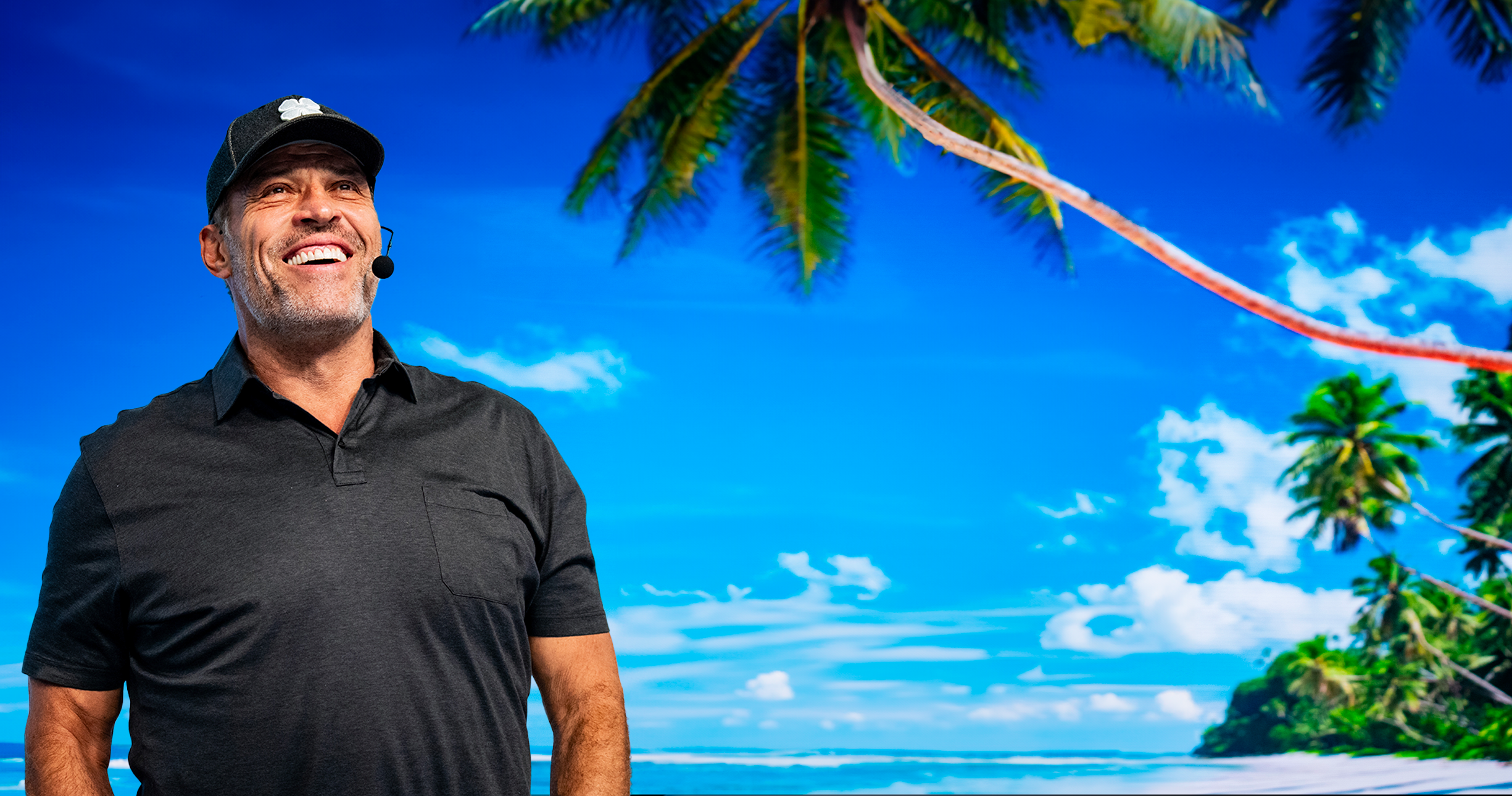 a man stands in front of a screen displaying a beach with palm trees