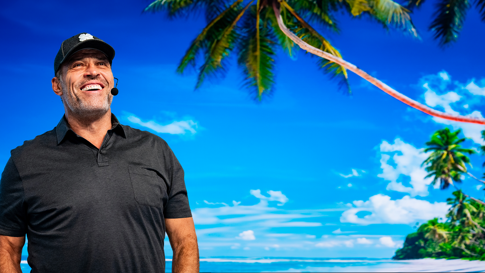 a man stands in front of a screen displaying a beach with palm trees