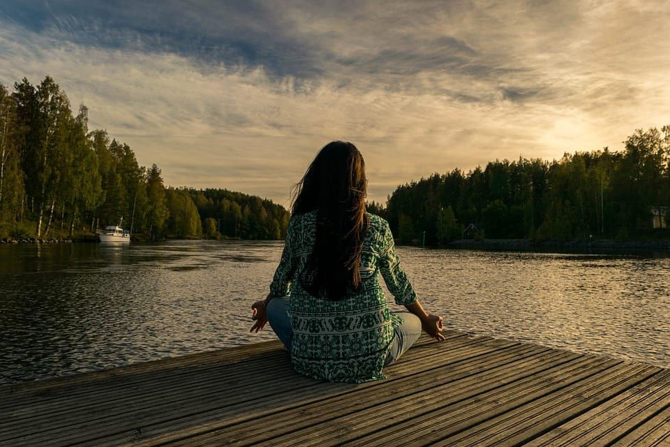 a woman is sitting on a dock meditating in front of a lake .