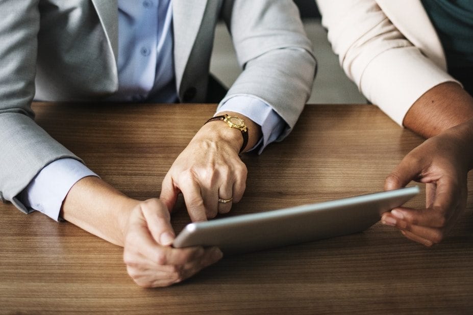 two women are sitting at a table looking at a tablet .