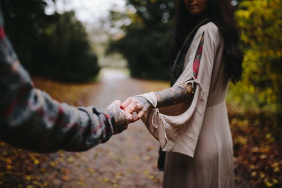 a man and a woman are holding hands in the woods .