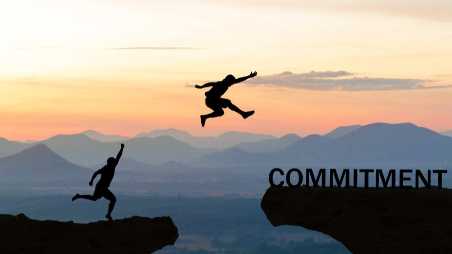 a man is jumping over a cliff with the word commitment in the background .
