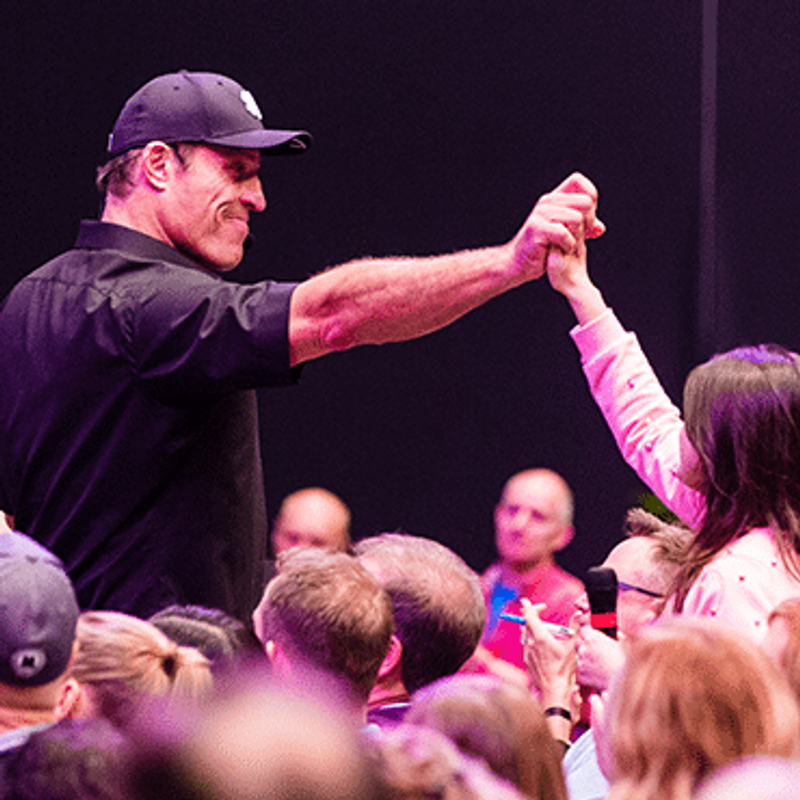 Stop living in fear of being hurt image of Tony Robbins grasping woman's hand in celebration