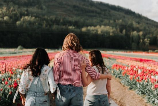three women are walking through a field of tulips .
