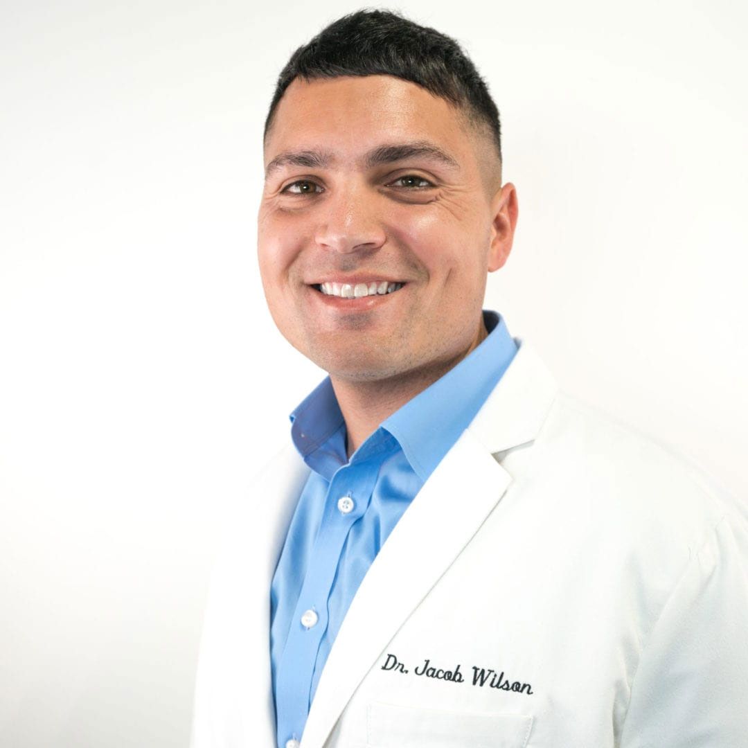 a man wearing a white lab coat and a blue shirt is smiling for the camera .