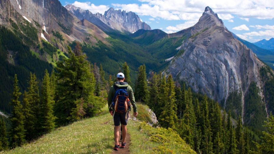 a man with a backpack is walking on a trail in the mountains .