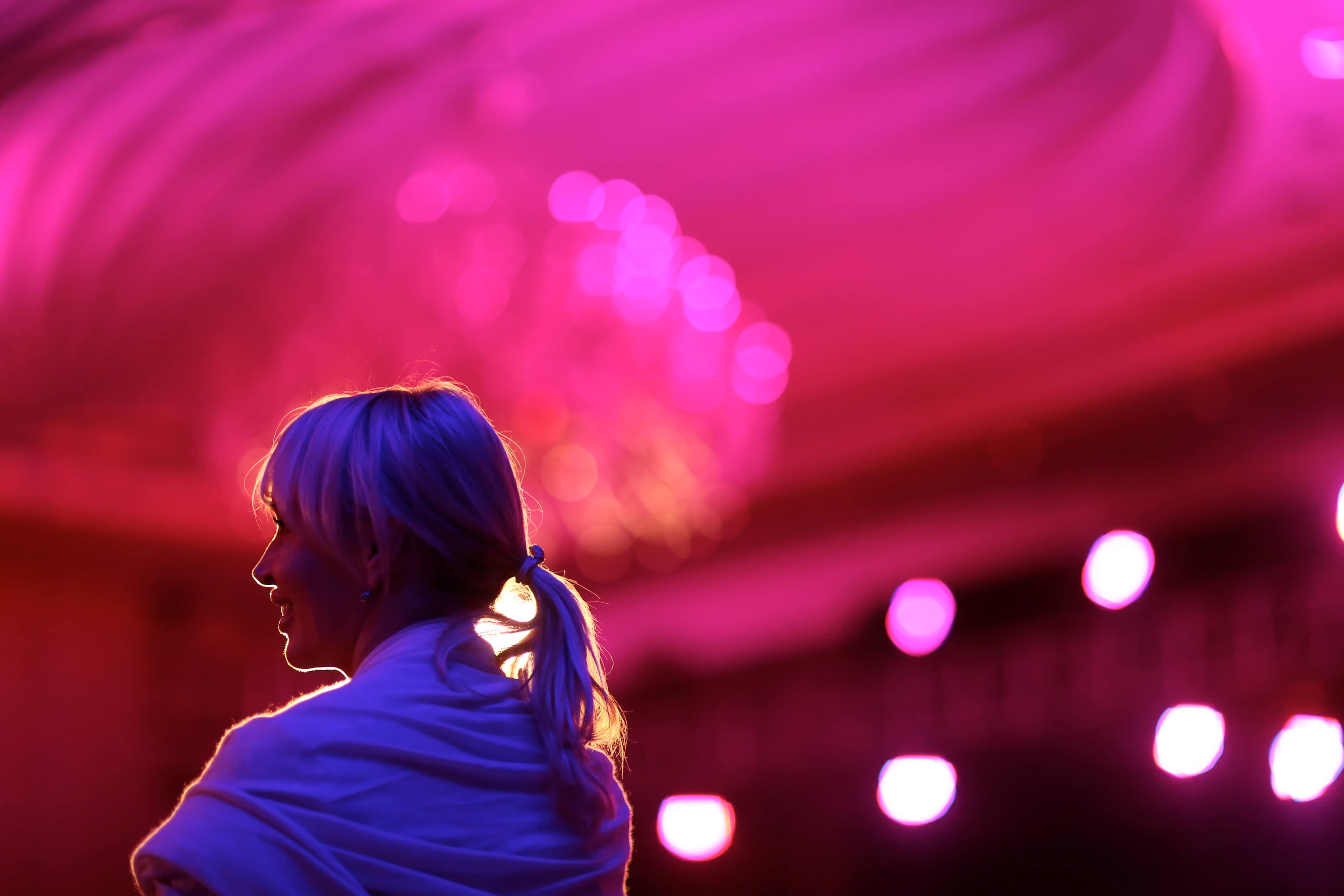 a woman is standing in front of a pink chandelier in a dark room .