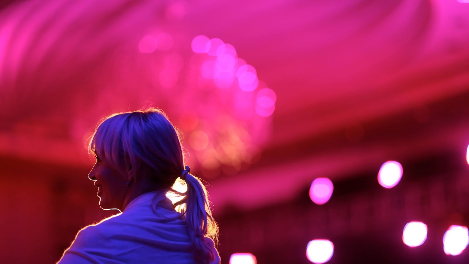 a woman is standing in front of a pink chandelier in a dark room .