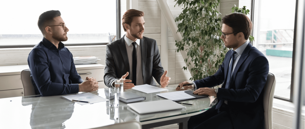 three men are sitting around a table having a conversation