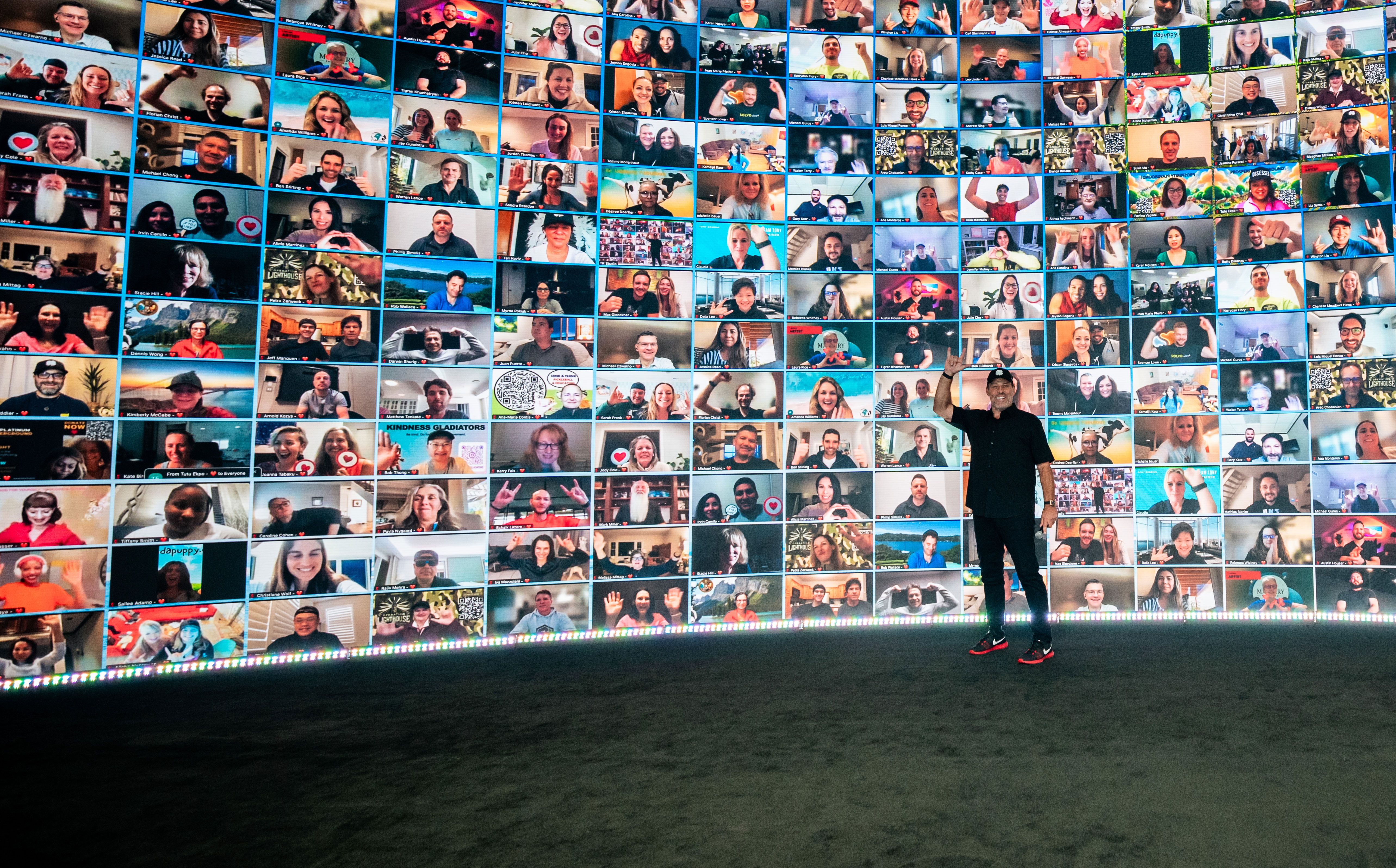 a man is standing in front of a wall filled with lots of pictures of people .