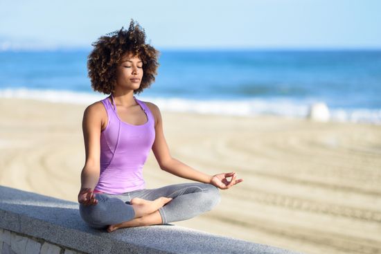a woman is sitting in a lotus position on the beach with her eyes closed .