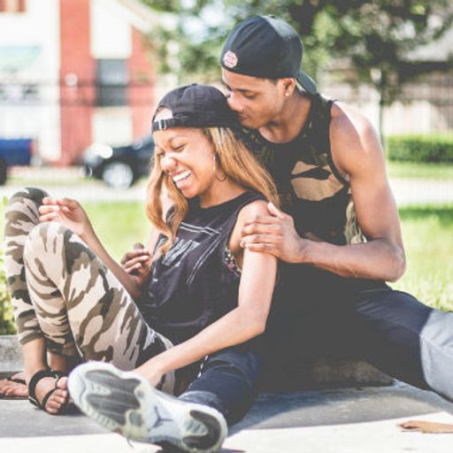 a man is kissing a woman on the cheek while they sit on the sidewalk .