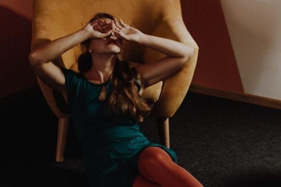 a woman in a green dress and red tights is sitting in a chair covering her face with her hands .
