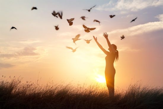 a woman is standing in a field with her arms outstretched and birds flying around her .
