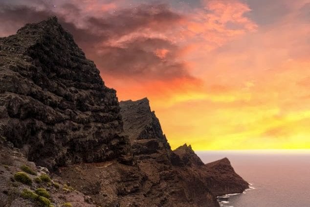 a cliff overlooking the ocean with a sunset in the background .