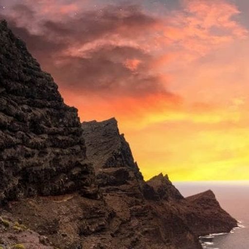 a cliff overlooking the ocean with a sunset in the background .