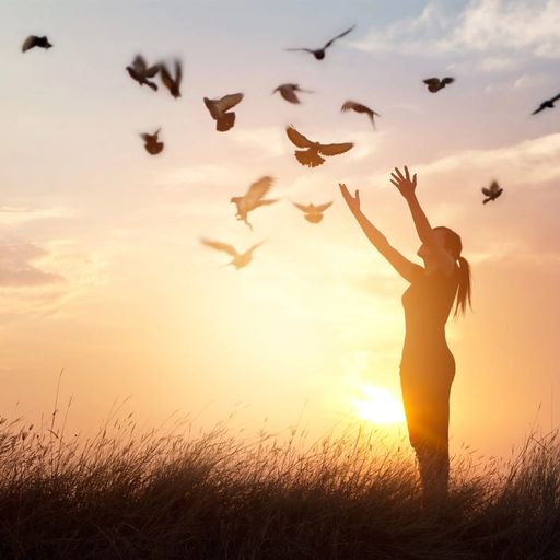 a woman is standing in a field with her arms outstretched and birds flying around her .