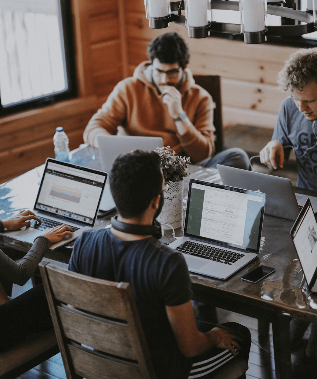 Four people work on laptops around a wooden table.