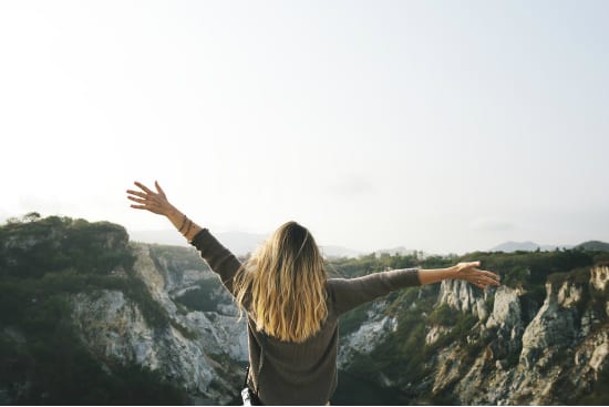 a woman is standing on top of a mountain with her arms outstretched .