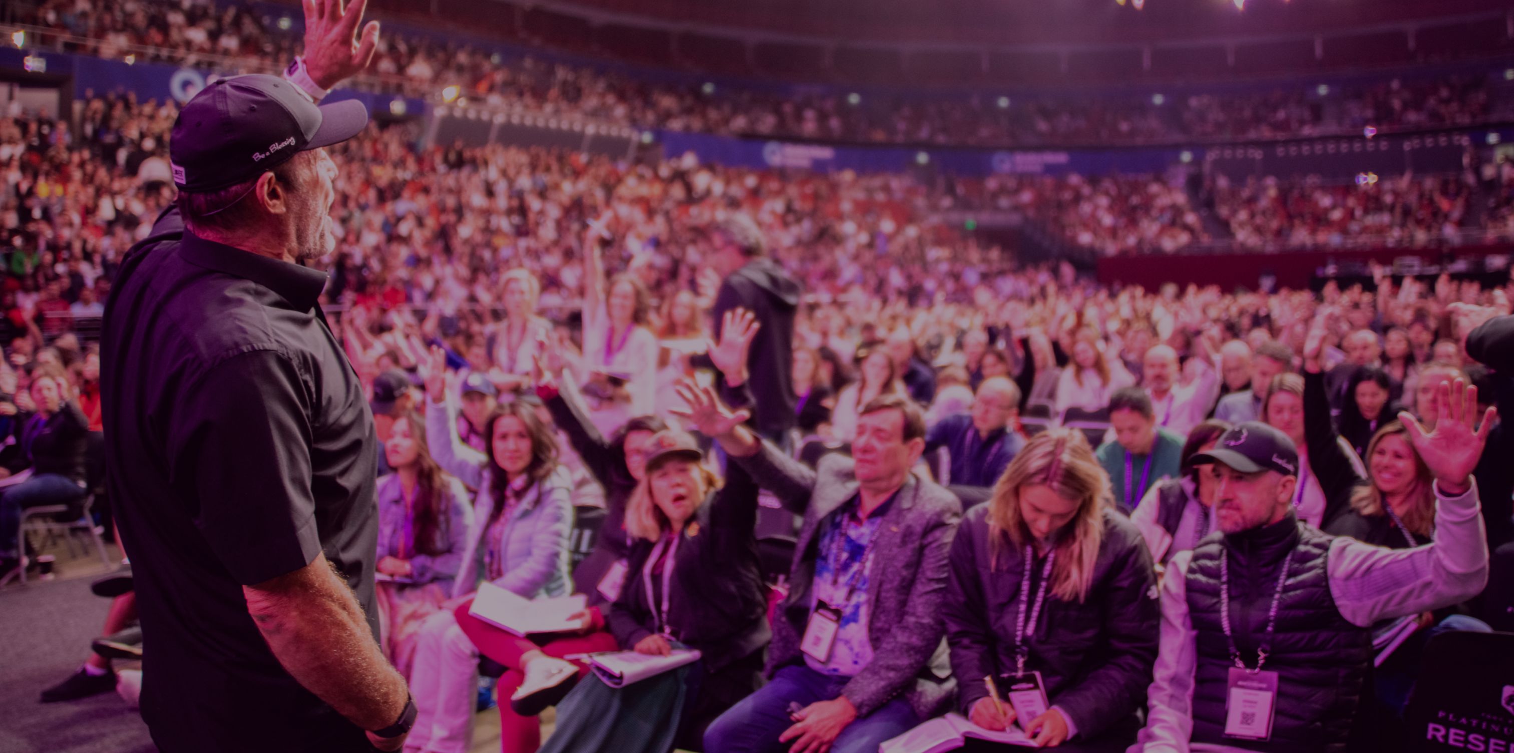 a man is standing in front of a crowd of people raising their hands in the air .