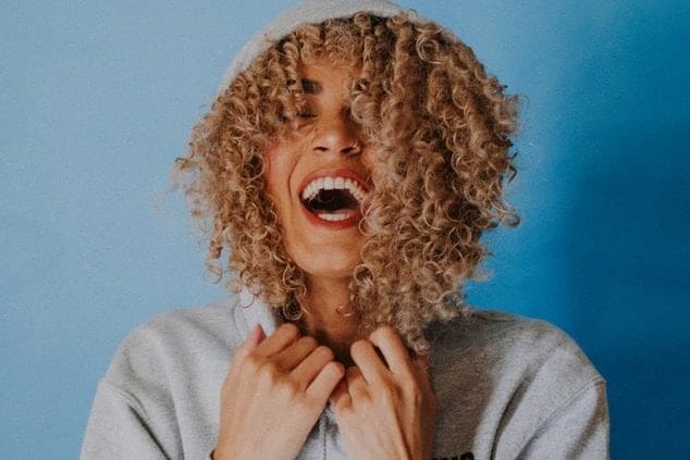 a woman with curly hair is laughing with her mouth open .