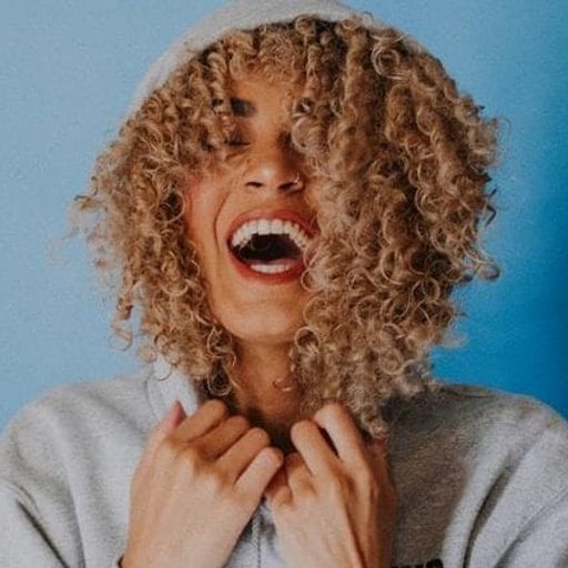 a woman with curly hair is laughing with her mouth open .