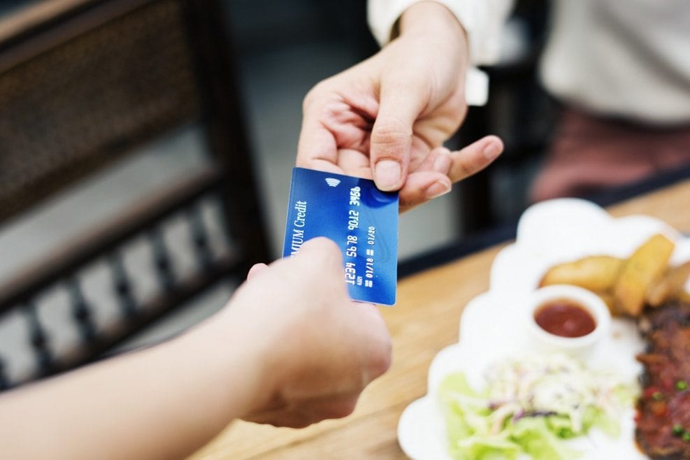 a person is handing a credit card to another person in front of a plate of food .