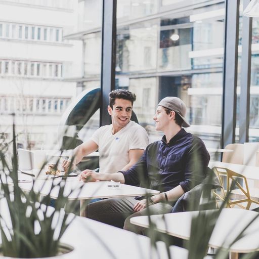 two men are sitting at a table in a cafe talking to each other .