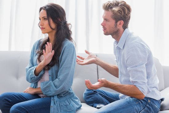 a man and a woman are sitting on a couch having an argument .