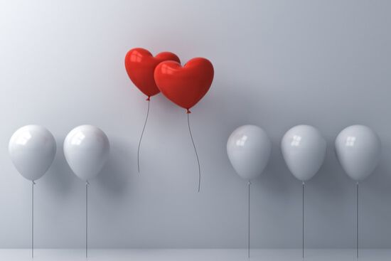 three red heart shaped balloons are flying in a row of white balloons .