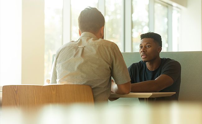 two men are sitting at a table having a conversation .