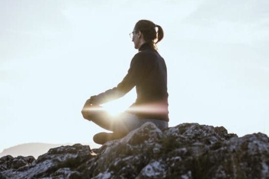 a woman is sitting in a lotus position on top of a rocky hill .