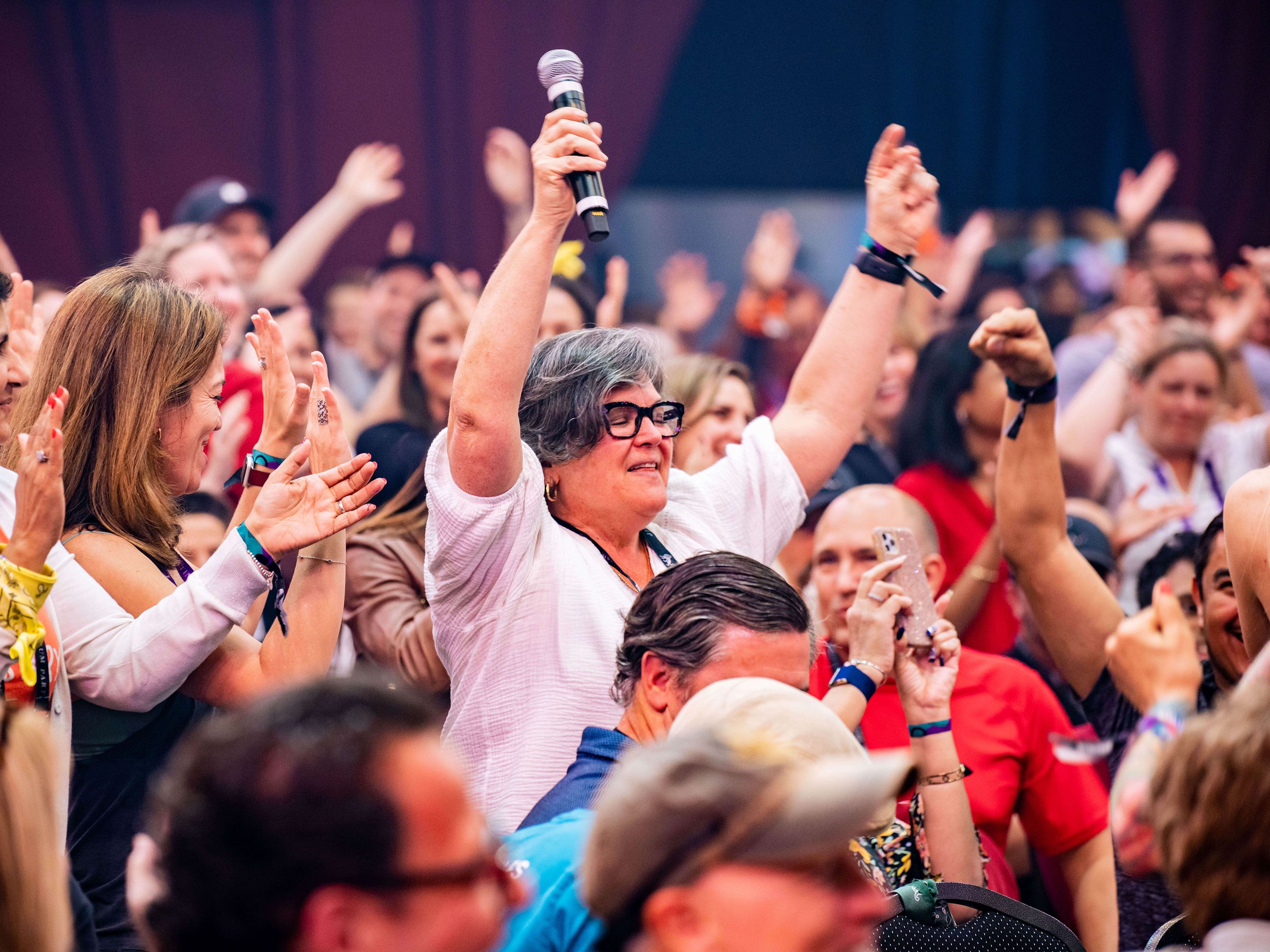 a woman is holding a microphone in front of a crowd of people .